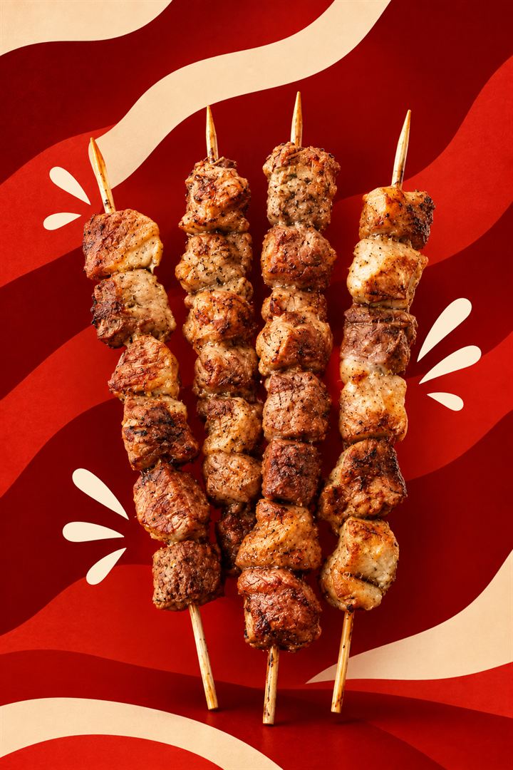 Quatro espetos de carne assados sobre fundo vermelho
